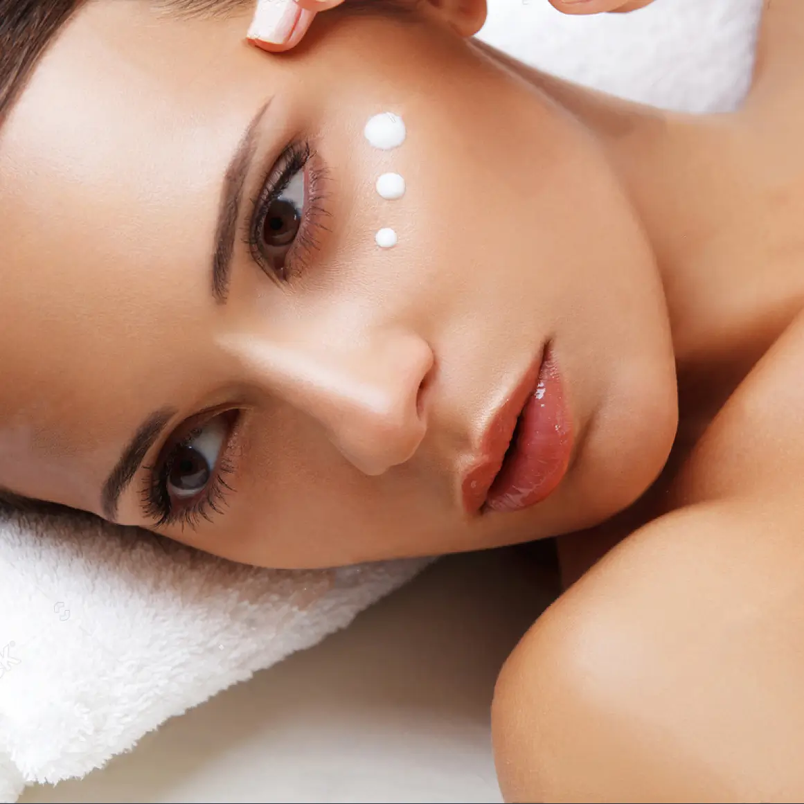 Primer plano de rostro de mujer con puntos de crema hidratante aplicados en pómulos y frente.