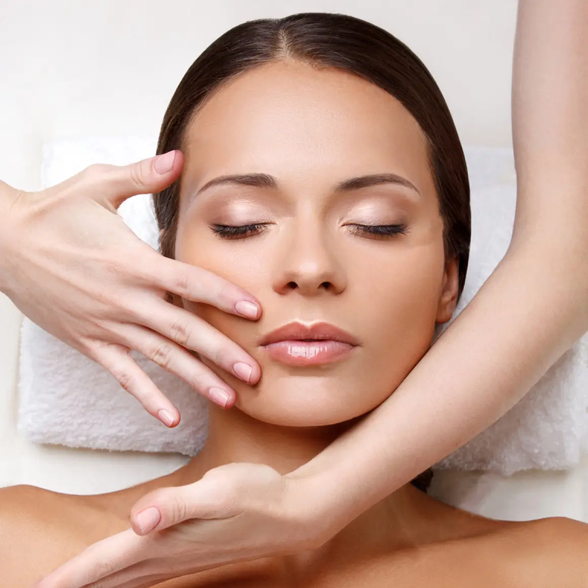 Manos de terapeuta realizando maniobras de masaje reafirmante en el óvalo facial de una mujer.